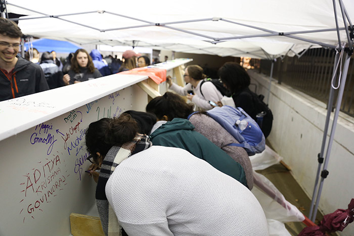 Half a dozen students stand in a row, adding their names to the steel beam.